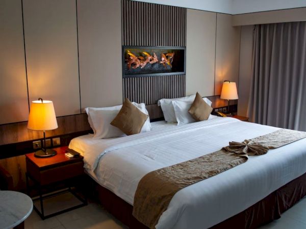 A hotel room featuring a king-sized bed, two bedside tables with lamps, and a decorative piece above the bed, creating a cozy ambiance.