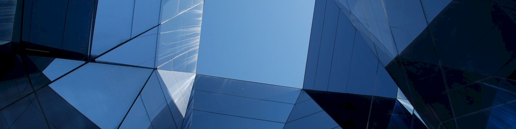 The image shows modern architectural structures with reflective glass panels, creating geometric patterns against a blue sky.