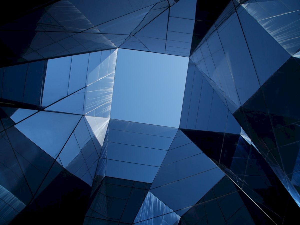 Abstract view of a modern building with reflective glass panels forming geometric patterns against a blue sky.