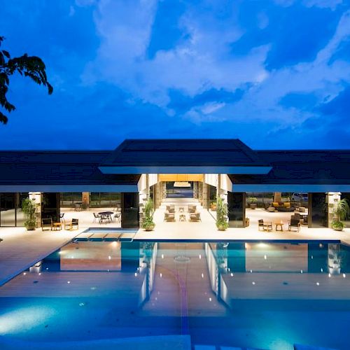 A luxurious modern building with a large illuminated pool in the foreground, set against a vibrant evening sky.