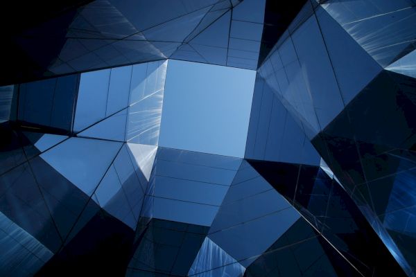 Geometric architecture with a central blue sky opening, surrounded by reflective glass panels, creating an abstract symmetrical view.