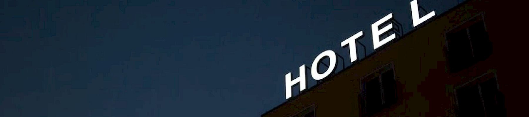 A building at night with an illuminated sign reading "HOTEL" on the roof against a dark sky.