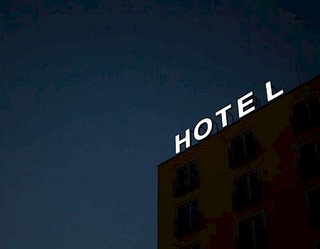 A building at night with an illuminated sign reading "HOTEL" on the roof against a dark sky.