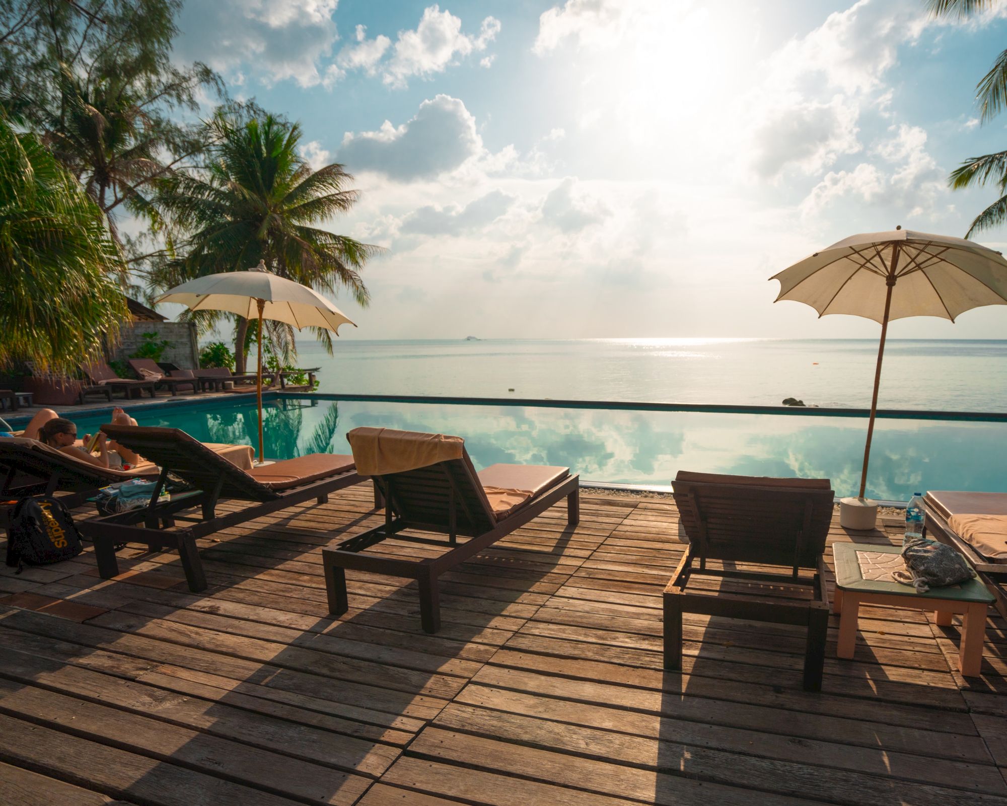 A serene beachside scene with lounge chairs, umbrellas, palm trees, and a view of the ocean under a sunny sky.