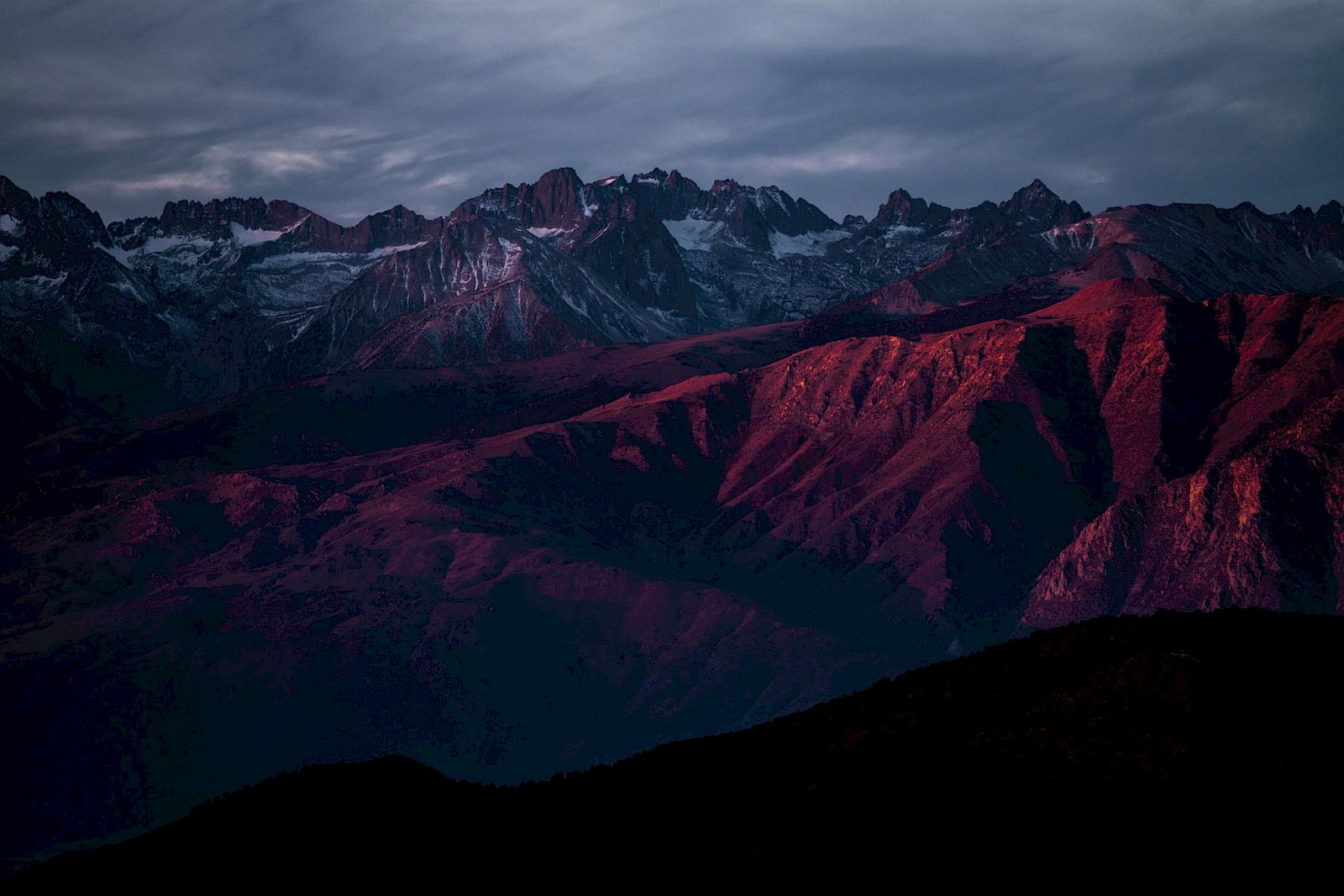 A mountain range illuminated by red sunset light under a cloudy sky, creating a dramatic and picturesque landscape.