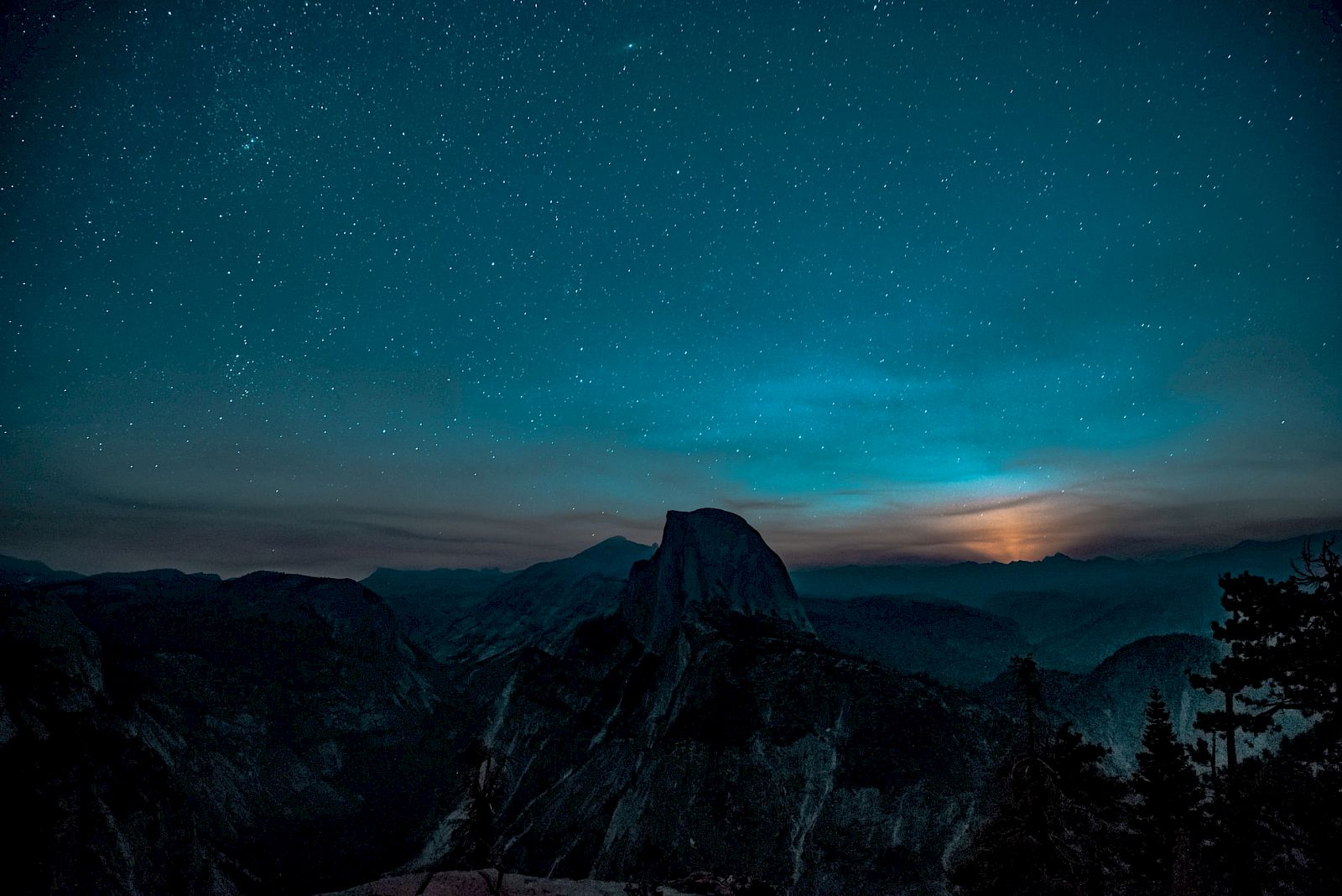 A starry night sky over a mountainous landscape with a horizon glow, creating a serene and mysterious atmosphere.