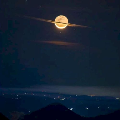 A full moon appears with clouds forming a ring-like shape around it, resembling Saturn, with a dark landscape below.