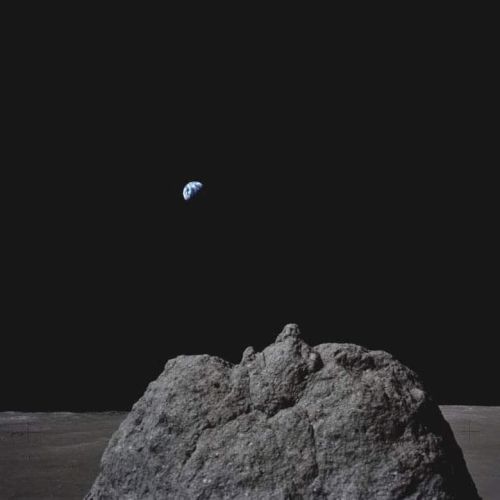 A view from the lunar surface showing Earth rising in the distance above a rocky landscape under a dark sky.
