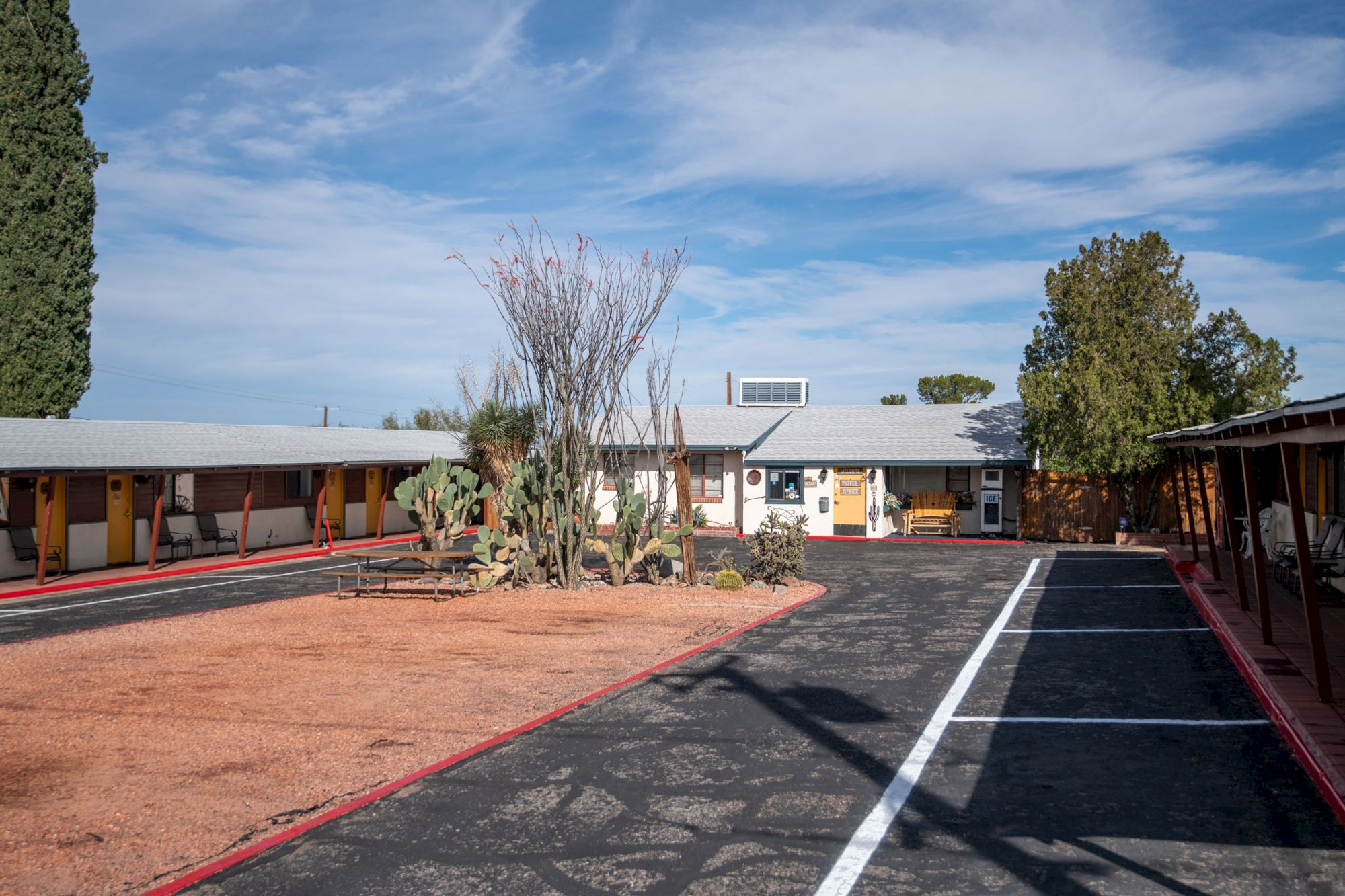 A motel courtyard with cacti, a central office, and shaded seating areas under a clear blue sky.