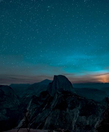 A starlit night sky over a mountainous landscape, with a glowing horizon creating a serene and mystical atmosphere.