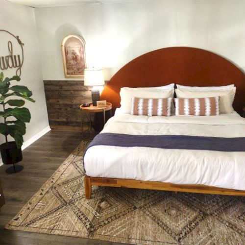 A cozy bedroom with a double bed, rustic decor, a "Howdy" sign, and a plant in the corner, creating a welcoming atmosphere.