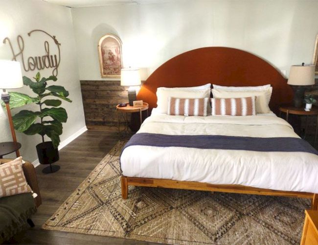 A cozy bedroom with a double bed, rustic decor, a "Howdy" sign, and a plant in the corner, creating a welcoming atmosphere.