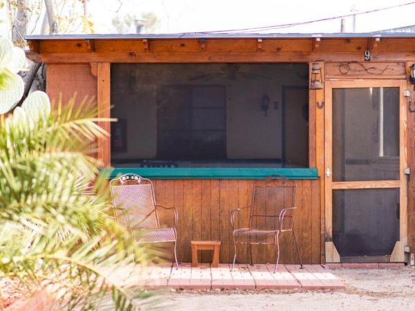 A small rustic cabin with a screened porch and two metal chairs outside on a brick pathway.