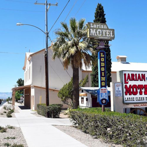 A street view of Larian Motel with signs advertising lodging; there's a road, sidewalk, and desert plants under a clear blue sky.