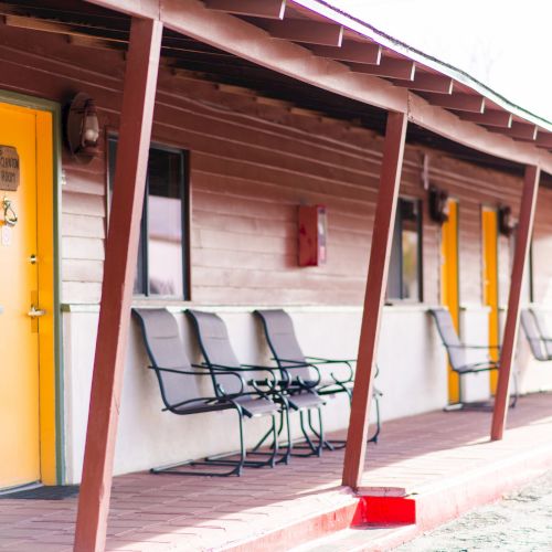 The image shows a motel exterior with yellow doors, rocking chairs, and a long covered walkway.