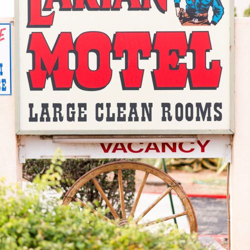 The image shows a sign for "Larian Motel" advertising "Large Clean Rooms" with a western-themed design including a cowboy graphic.