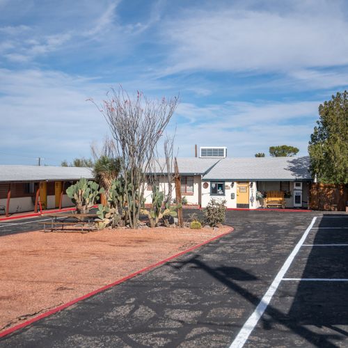 The image shows a rustic motel courtyard with a central garden featuring desert plants, surrounded by single-story buildings under a blue sky.