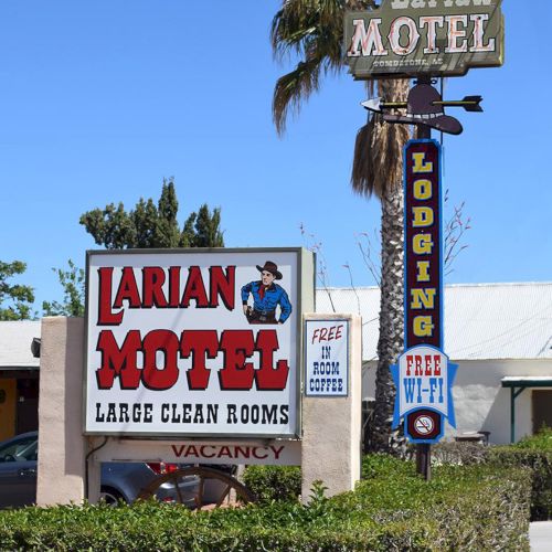 The image shows signage for Larian Motel offering large clean rooms, free Wi-Fi, and in-room coffee, set against a clear blue sky.