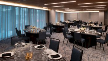 The image shows an elegant banquet hall with round tables, set for an event with plates, glasses, napkins, and floral centerpieces.