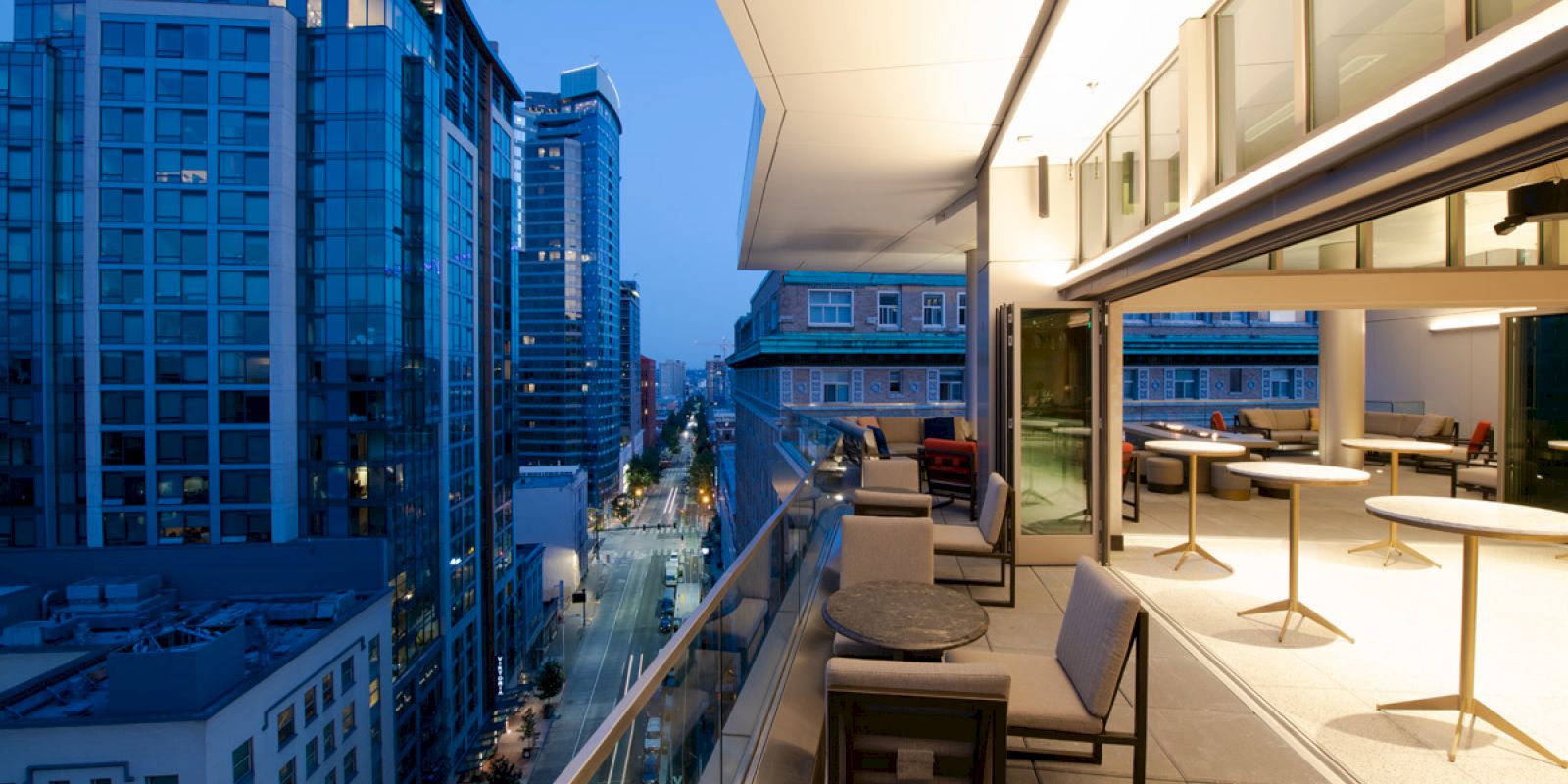 A modern cityscape at dusk with a view from a balcony, featuring tall buildings and a stylish outdoor seating area.