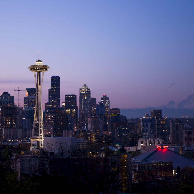 Seattle skyline at dusk featuring the Space Needle, city buildings, and Mount Rainier in the background under a purple sky.