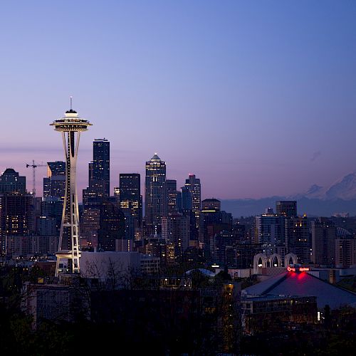 The image shows Seattle's skyline at dusk, featuring the Space Needle and Mount Rainier in the background under a clear sky.