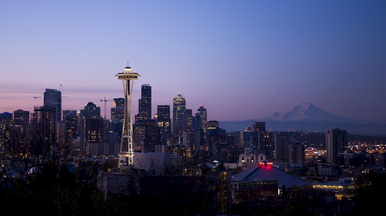 Seattle skyline with the Space Needle at dusk and Mount Rainier in the background, featuring city lights and a purple sky.
