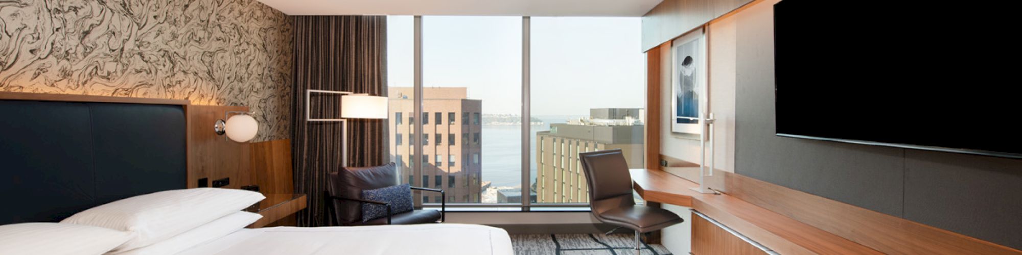A modern hotel room features a large bed, a desk, and a wall-mounted TV, with a cityscape view through the window.